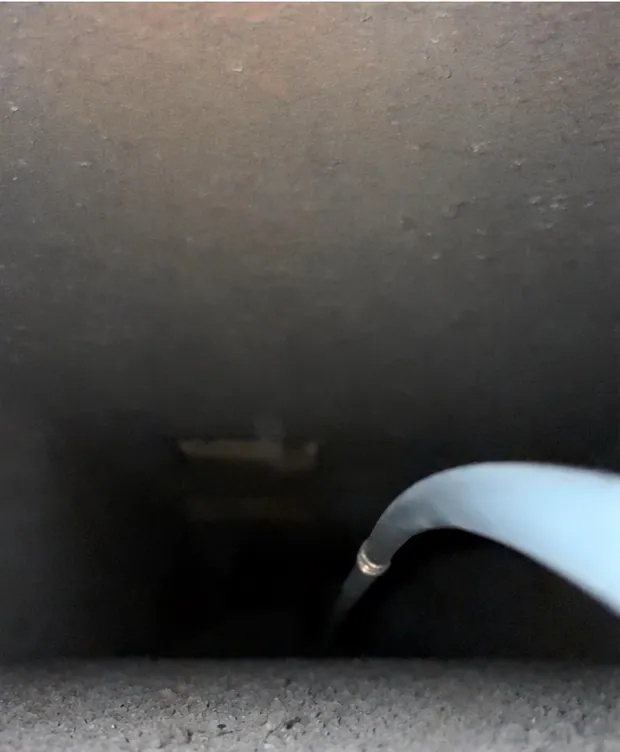 A duct run before cleaning, with grey buildup along the bottom and the cleaning hose in the run